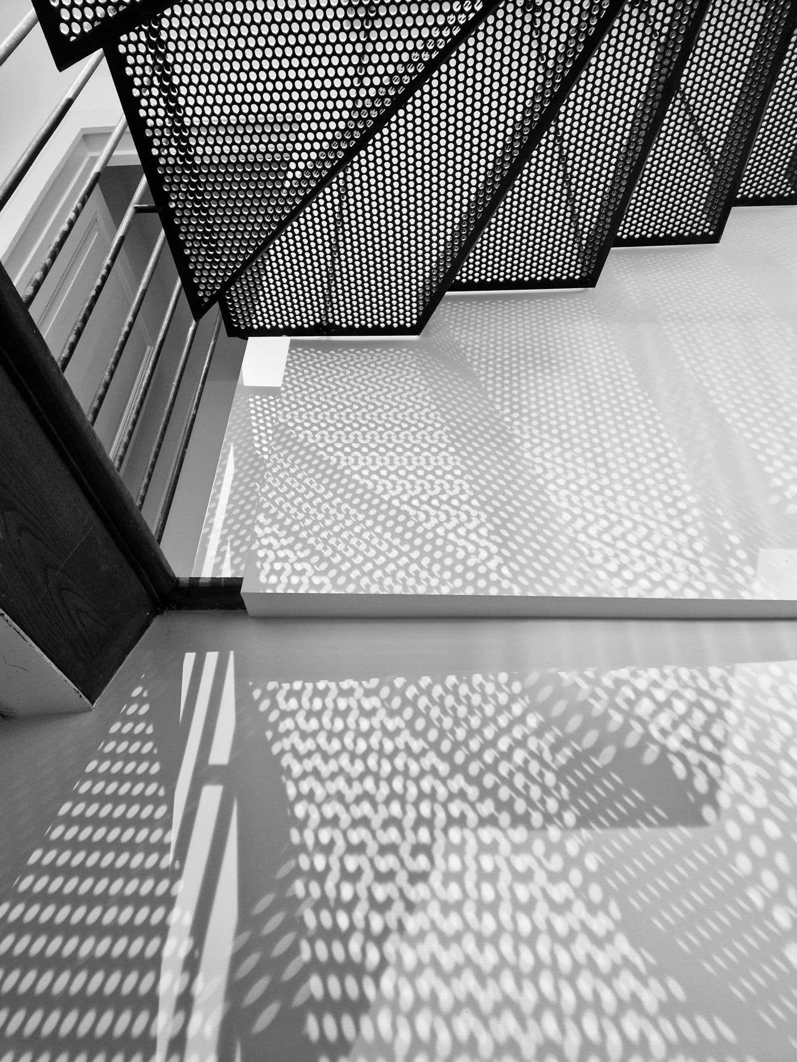 Escalier métal perforé maison de village — ombres dentelles projetées au sol